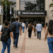 Candidatos caminham em direção à prefeitura com mochilas e documentos de concurso público.